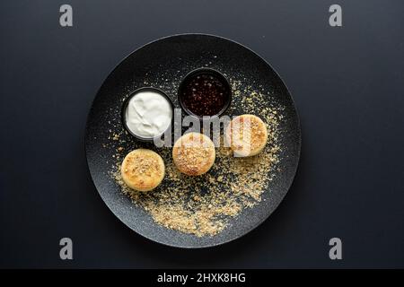 Quark Käsekuchen auf einem schwarzen Teller mit saurer Rahm und Marmelade Stockfoto