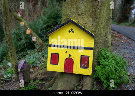 Gelbe und rote Feentür, die an der Basis eines Baumstammes in einem irischen Waldmärchen-Garten befestigt ist. Stockfoto