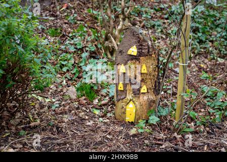 Hohes hölzernes Feenhaus mit gelben Fenstern und Feentür, aus Baumstumpf im irischen Waldmärchengarten. Stockfoto