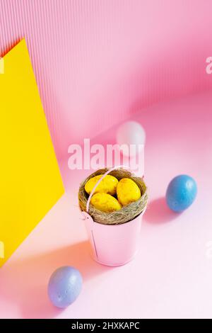 Gelbe ostereier im rosa Eimer. Ostereier in einem Nest auf einem rosa-gelben Hintergrund. Speicherplatz kopieren Stockfoto