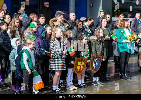 Warrington, Hes. 13. März 2022. Der Warrington Irish Club ist Gastgeber des Services und des Starts der St. Patrick's Day Parade. Dies ist die erste Parade seit dem Start von COVID. Beginnend um 10,30 Uhr morgens vom Irish Club in Orford Lane zum ‘River of Life' in der Bridge Street im Stadtzentrum, wo ein kurzer Gottesdienst abgehalten wurde, um an den Jahrestag des Bombenanschlags von Warrington zu erinnern. Es regnete, sobald die Parade begann und dann kam die Sonne heraus. Kinder hören dem Service zu. Quelle: John Hopkins/Alamy Live News Stockfoto