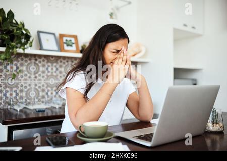 Ich brauche nur eine Minute. Aufnahme einer jungen Frau, die gestresst aussieht, während sie zu Hause an einem Laptop arbeitet. Stockfoto