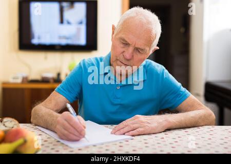 Fokussierter Senior beim Lesen und Unterzeichnen von Papieren am Tisch Stockfoto