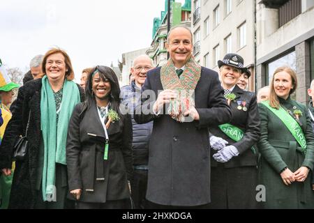 London, Großbritannien. 13. März 2022. Micheál Martin, irischer Premierminister, führt an der Front der Londoner St. Patrick's Day Parade mit einem Schal in ukrainischen Farben, zusammen mit Dr. Debbie Weekes-Bernard, der stellvertretenden Bürgermeisterin, den Gemeinden und der sozialen Gerechtigkeit auf seiner linken Seite, seiner Frau Mary, Und Pandemiearbeiter, die als Großmarschall für die Parade geehrt wurden. Kredit: Imageplotter/Alamy Live Nachrichten Stockfoto