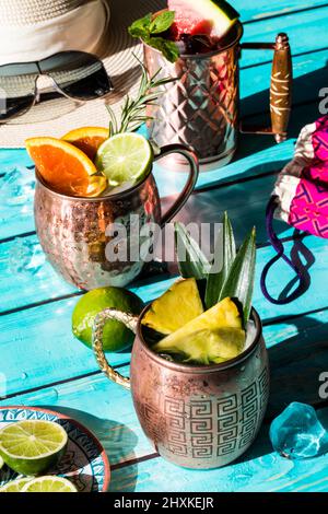 Drei Sommercocktails, garniert mit frischem Obst und Kräutern bei hellem Sonnenlicht. Stockfoto