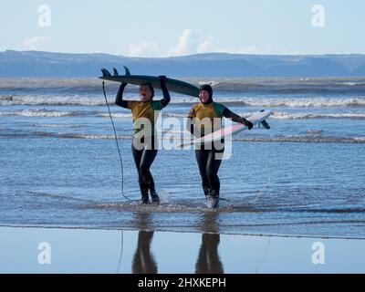 Zwei Surfer der Surfschule kommen aus dem Meer, Westward Ho!, Devon, Großbritannien Stockfoto