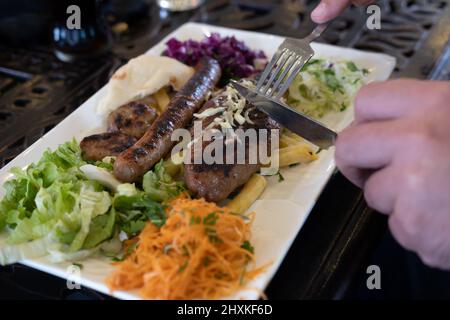 Verschiedene Arten von gegrilltem oder gegrilltem Fleisch auf dem Teller, Schneiden und Schneiden Fleischbällchen mit Käse und Wurst mit Gemüsesalat und pommes frites Stockfoto