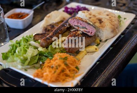 Verschiedene Arten von gegrilltem oder gegrilltem Fleisch, Fleischbällchen mit Käse und Wurst mit Gemüsesalat auf dem Teller Stockfoto