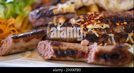 Verschiedene Arten von gegrilltem oder gegrilltem Fleisch, Fleischbällchen mit Käse und Wurst mit Gemüsesalat auf dem Teller Stockfoto