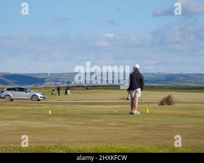 Golfer, der auf dem Abschlag wartet, während das Auto über das Grob fährt, der Royal North Devon Golf Club, Westward Ho, Devon, Großbritannien Stockfoto