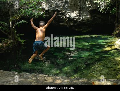 Rückansicht eines mexikanischen Teenagers, der im Wald in Mexiko in eine Cenote springt Stockfoto