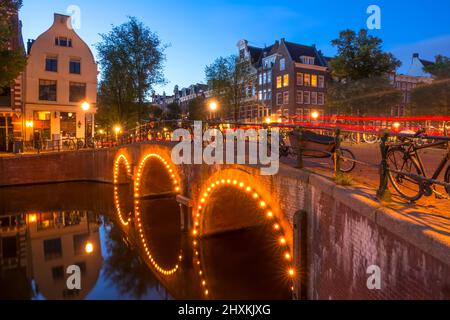 Niederlande. Steinbrücke mit drei Bögen auf dem Amsterdamer Kanal. Viele geparkte Fahrräder. Ende der Nacht Stockfoto