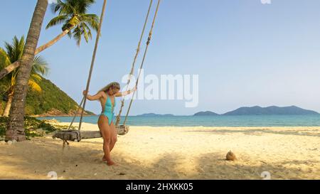 Hübsche Frau, die auf einer Schaukel an einem tropischen Strand, am Ufer des türkisfarbenen Meeres, schwingt. Konzept Reisen, Spaziergänge, Erholung im Meer, tropische Resort Küste Entspannung Reisen Tourismus Sommerferien Stockfoto