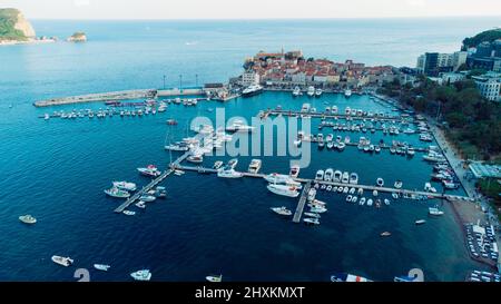 Luftaufnahme von oben nach unten von Bootsanlegestelle und Yachthafen in Budva, Montenegro. Weiße private Motorboote werden an der adriatischen Küste an der Anlegestelle vertäut. Yachtclub Stockfoto