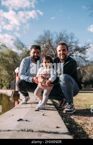 Porträt einer modernen Familie im Park mit zwei männlichen Eltern und einem kleinen Mädchen Stockfoto