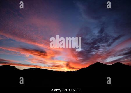 Silhouette von abgerundeten Bergen unter dem herrlichen Sonnenuntergangshimmel von rosa, orange, rot, mauve und gelb über Starr Pass, Tucson, Arizona Stockfoto