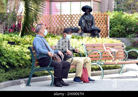 (220314) -- HONGKONG, 14. März 2022 (Xinhua) -- maskierte Menschen sitzen auf einer Bank im südchinesischen Hongkong, 13. März 2022. Am Sonntag registrierte Hongkong 13.335 neue COVID-19-Fälle durch Nukleinsäuretests und 19.095 weitere positive Fälle durch selbst berichtete Schnellantigen-Tests, wie offizielle Daten zeigten. (Xinhua/Lo Ping Fai) Stockfoto