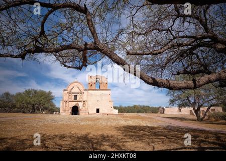 Mission San Jose de Tumacacori im Tumacácori National Historical Park, eingerahmt von Bäumen und seinem Schatten Stockfoto