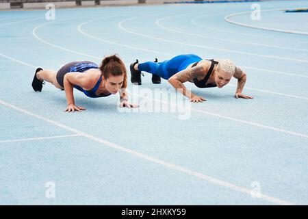 Du bist bereit. Ganzkörperaufnahme von zwei attraktiven jungen Sportlerinnen, die Liegestütze auf der Strecke machen. Stockfoto