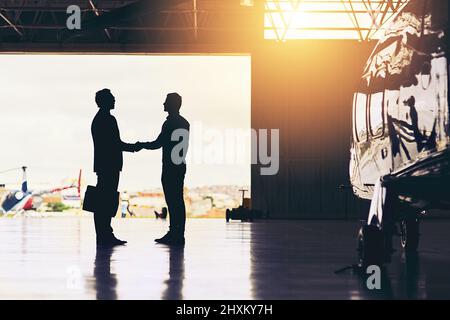 Willkommen zu Hause. In voller Länge Aufnahme von zwei nicht erkennbaren Geschäftsleuten, die sich beim Stehen in einem Kleiderbügel am Flughafen die Hände schüttelten. Stockfoto