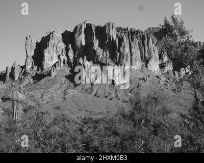 Schwarz-weiße Wüstenlandschaften in Arizona. Gezeigt werden der Superstition Mountain und seine „betende Hände“-Formation sowie ein Mond über dem Wüstenberg. Stockfoto