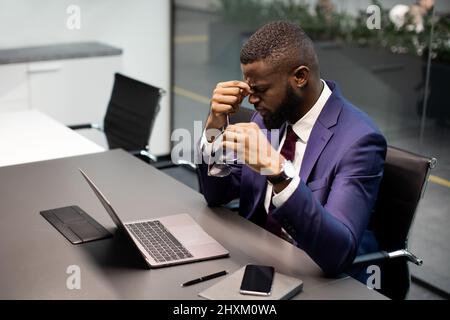 Müder schwarzer CEO, der im Büro arbeitet und Migräne hat Stockfoto