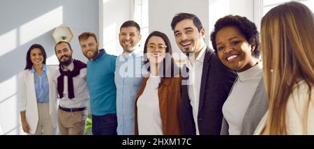 Multirassisches Team glücklicher junger Geschäftsleute, die sich in ihrem Büro umarmen und lächeln Stockfoto