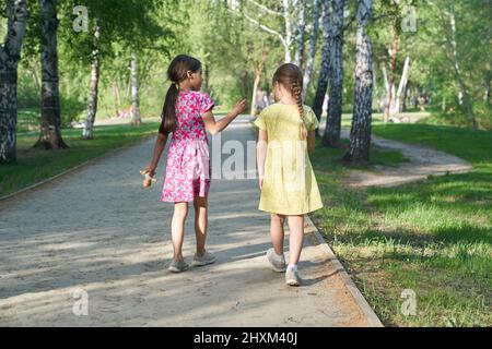 Ein Foto von hinten von zwei kleinen Schwestern, die gemeinsam auf einem Pfad im Park spazieren gehen. Das Konzept der Liebe und Freundschaft der Kinder, beste Freunde für immer. Hochwertige Fotos Stockfoto