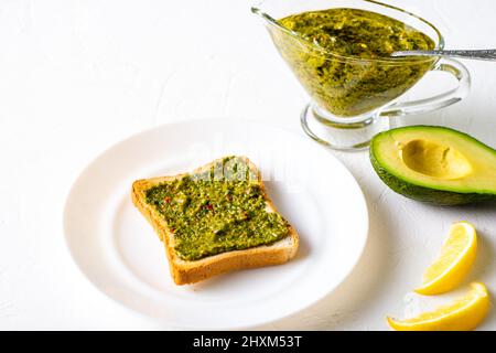 Toast mit Avocado und Chimichurri-Sauce auf einem weißen Teller. Gesundes vegetarisches Essen. Weißer Hintergrund. Stockfoto