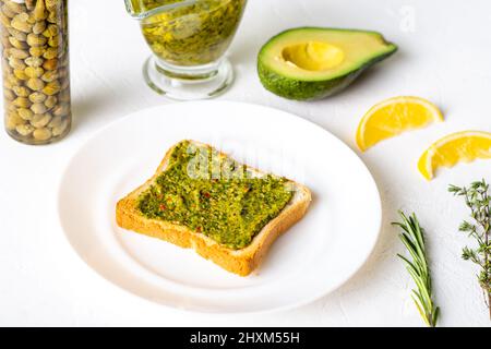 Toast mit Avocado und Chimichurri-Sauce auf einem weißen Teller. Gesundes vegetarisches Essen. Weißer Hintergrund. Stockfoto