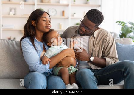 Afroamerikanische Eltern sitzen mit weinenden Jungen auf dem Sofa Stockfoto