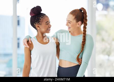 Freunde, die zusammen Yoga machen, bleiben zusammen. Aufnahme von zwei jungen Frauen, die nach dem Yoga-Üben eng beieinander stehen. Stockfoto
