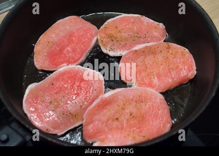 Fünf Stücke Schweinefleisch mit Pfeffer bestreut, in einer Pfanne auf einer Seite braten Stockfoto