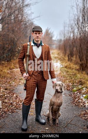 jäger im klassischen Anzug mit Hunden Jagd Vogel Holzhahn im Wald, mit Gewehr Schrotflinte. Brutaler Rüde mit ausgebildeten reinrassigen Hund in ländlicher Umgebung Tempo, Fores Stockfoto