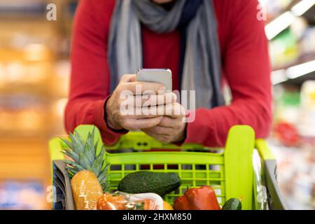 Ein Mann, der beim Einkaufen im Supermarkt Handy benutzte Stockfoto