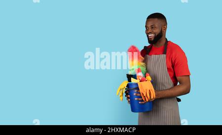 Reinigungsangebot. Black Male Cleaner Holding Basket Mit Waschmitteln Und Blick Zur Seite Stockfoto