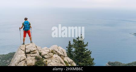 Junger Wanderer Backpacker Mann mit Trekkingstöcken genießen das Mittelmeer auf Clifftop während Lycian Way Trekking Walk. Berühmte Likya Yolu Türkisch Stockfoto