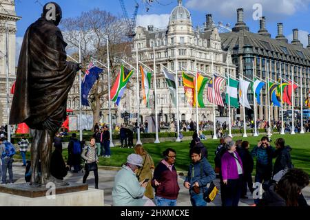 London, Großbritannien. 12.. März 2022. Die Statue von Mahatma Gandhi überblickt den Parliament Square, auf dem die Flaggen der 54 Mitgliedsstaaten des Commonwealth zur Feier des Commonwealth Day am 14.. März fliegen. Stockfoto