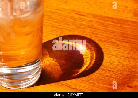 Licht und Schatten auf dem Tisch, wo die Sonne durch ein kaltes Glas Eis und Wasser scheint Stockfoto