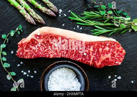 Marmoriertes japanisches Wagyu-Streifensteak mit grünen Kräutern und Spargel Stockfoto