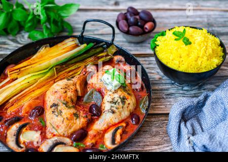 Im Ofen geröstete Hähnchenschenkel mit gegrilltem Lauch, Oliven und Pilzen in Tomatensauce, serviert mit Safranreis Stockfoto