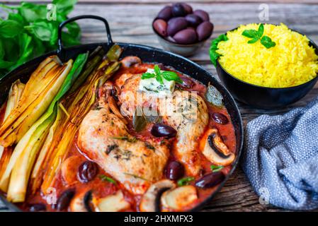 Im Ofen geröstete Hähnchenschenkel mit gegrilltem Lauch, Oliven und Pilzen in Tomatensauce, serviert mit Safranreis Stockfoto