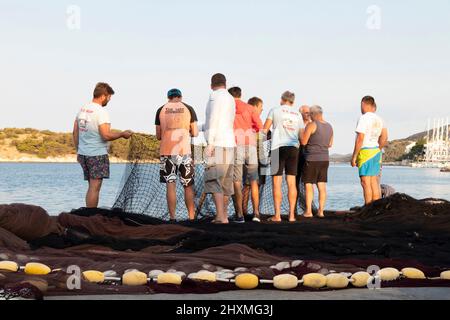 Tribunj, Kroatien - 23. August 2021: Gruppe von Fischern, die das Fischernetz am Küstendock reparieren Stockfoto
