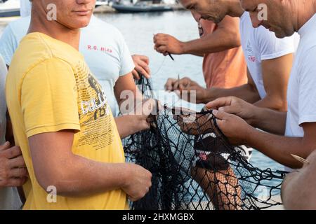 Tribunj, Kroatien - 23. August 2021: Gruppe von Fischern, die das Fischernetz reparieren, Nahaufnahme Stockfoto
