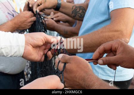 Tribunj, Kroatien- 23. August 2021: Gruppe von Fischern, die das Fischernetz reparieren, die Hände arbeiten, Details aus nächster Nähe Stockfoto