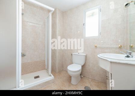 Badezimmer mit weißen Holzschränken, Duschkabine mit Bildschirm und kleinem Fenster in der Wand Stockfoto