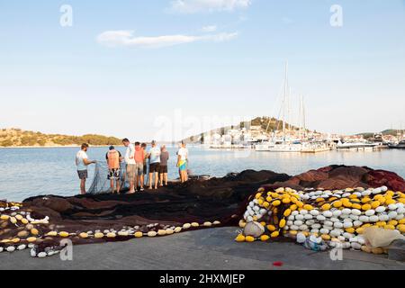 Tribunj, Kroatien - 23. August 2021: Gruppe von Fischern, die das Fischernetz am Küstendock reparieren Stockfoto