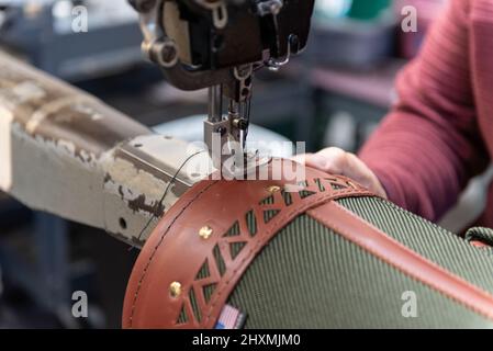 Qualifizierte Hände von Fabrikarbeitern, die den Stickfaden in der Produktion um den Rand der Ledertasche führen. Stockfoto