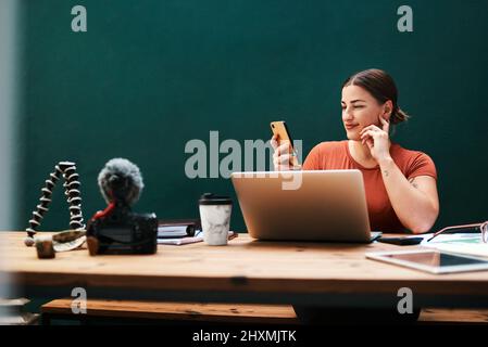 Dank Technologie kann ich von allen Geräten aus arbeiten. Ausgeschnittene Aufnahme einer attraktiven jungen Geschäftsfrau, die allein an ihrem Schreibtisch sitzt und ihr Handy benutzt. Stockfoto