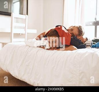 Einen weiteren dummen Moment gemeinsam zu teilen. Porträt zweier kleiner Brüder, die zu Hause auf einem Bett unter einem Wäschestapel liegen. Stockfoto